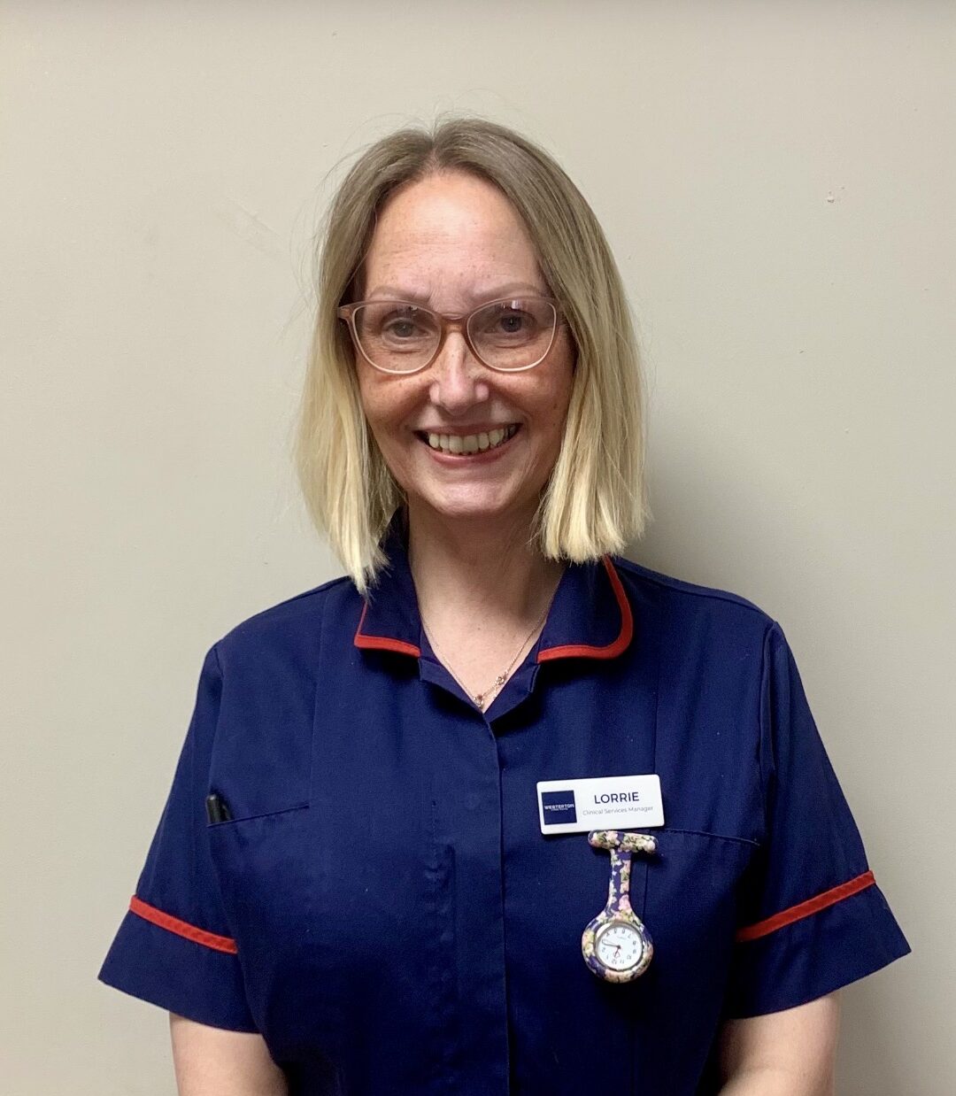 woman with blond bob smiling in a dark blue collared shirt
