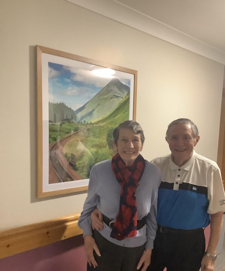 elderly couple smiling in a care home corridor